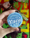 Hand holding a 'Pass the Yaoi' button in front of a colorful comic book background